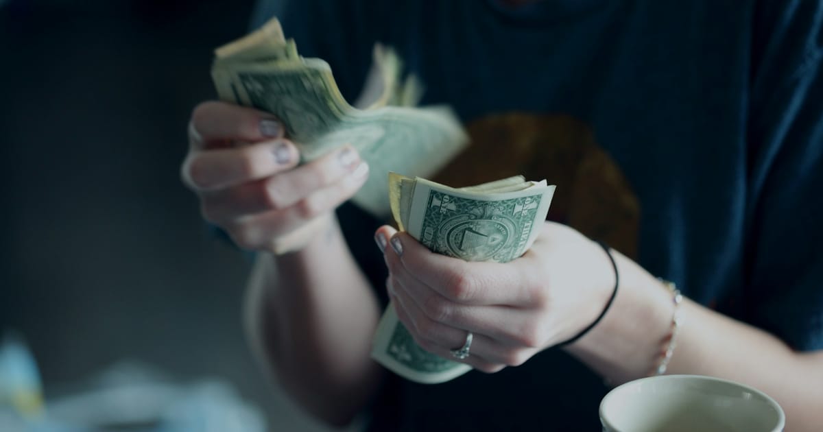 Una persona cuenta billetes de dólar con las dos manos.