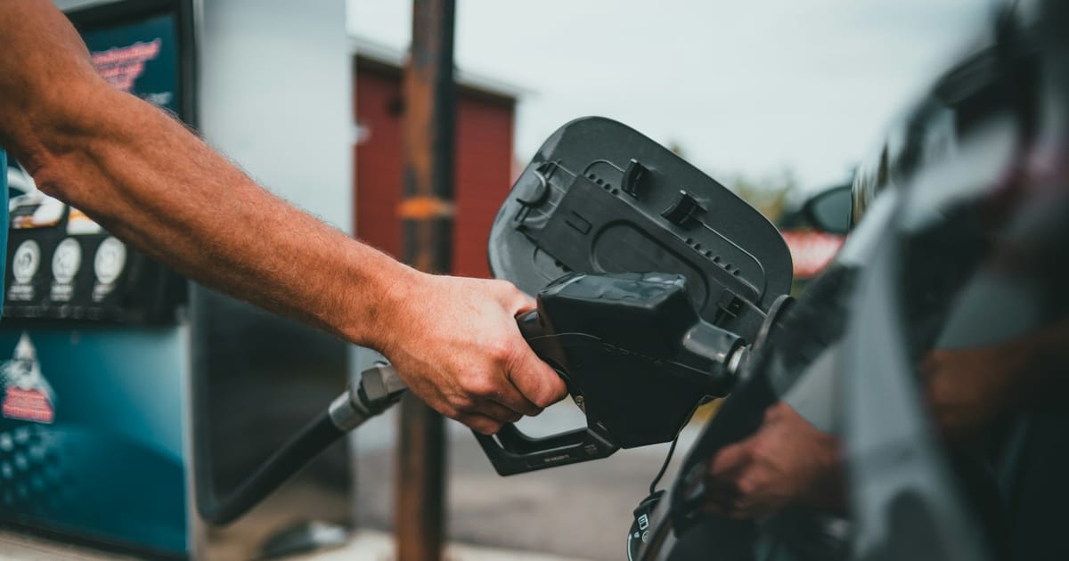Una persona carga combustible en un auto con la manguera del surtidor.