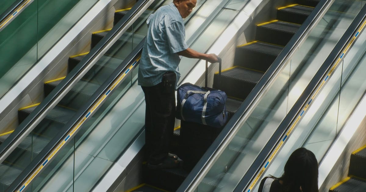 Un hombre con equipaje baja por una escalera mecánica en un aeropuerto.