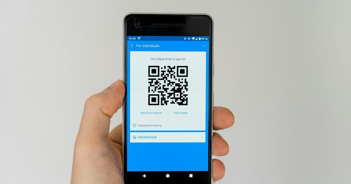 Una mano sostiene un celular que muestra un código QR en la pantalla.